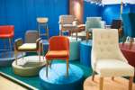 Display of various colorful chairs on platforms in a modern furniture showroom with a blue background