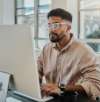 Man wearing glasses working at a desktop computer in a bright office environment