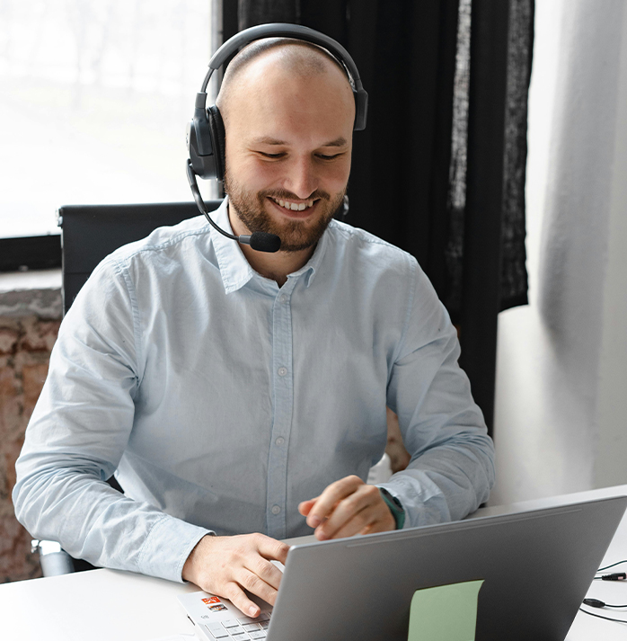 Smiling support representative wearing a headset, working on a laptop at a desk in a well-lit office